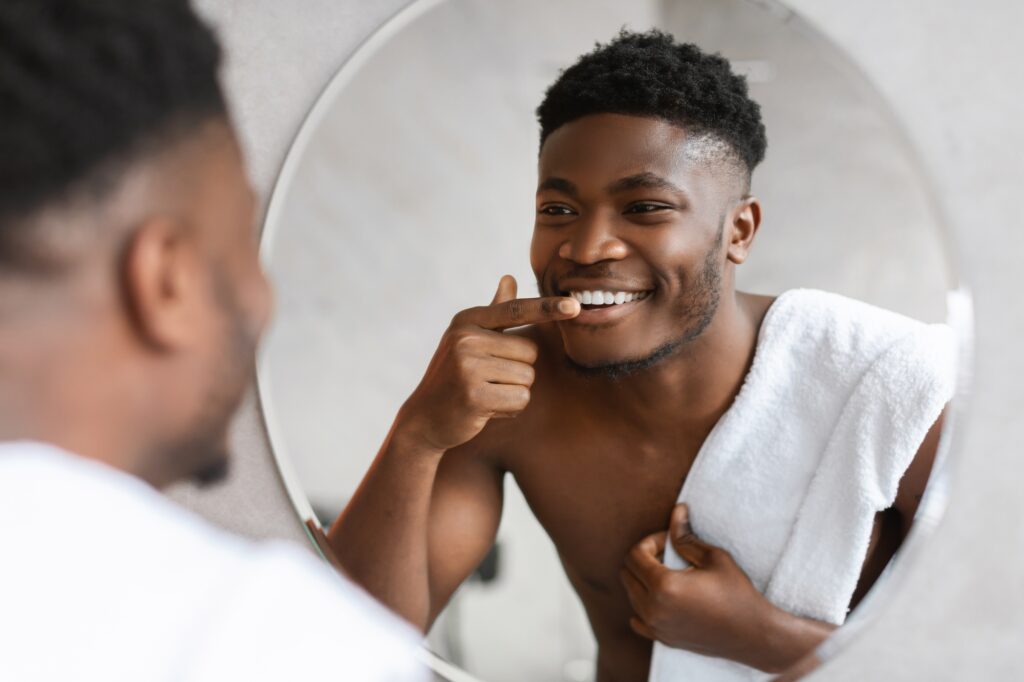Black Man Looking At His Smile In Mirror In Bathroom